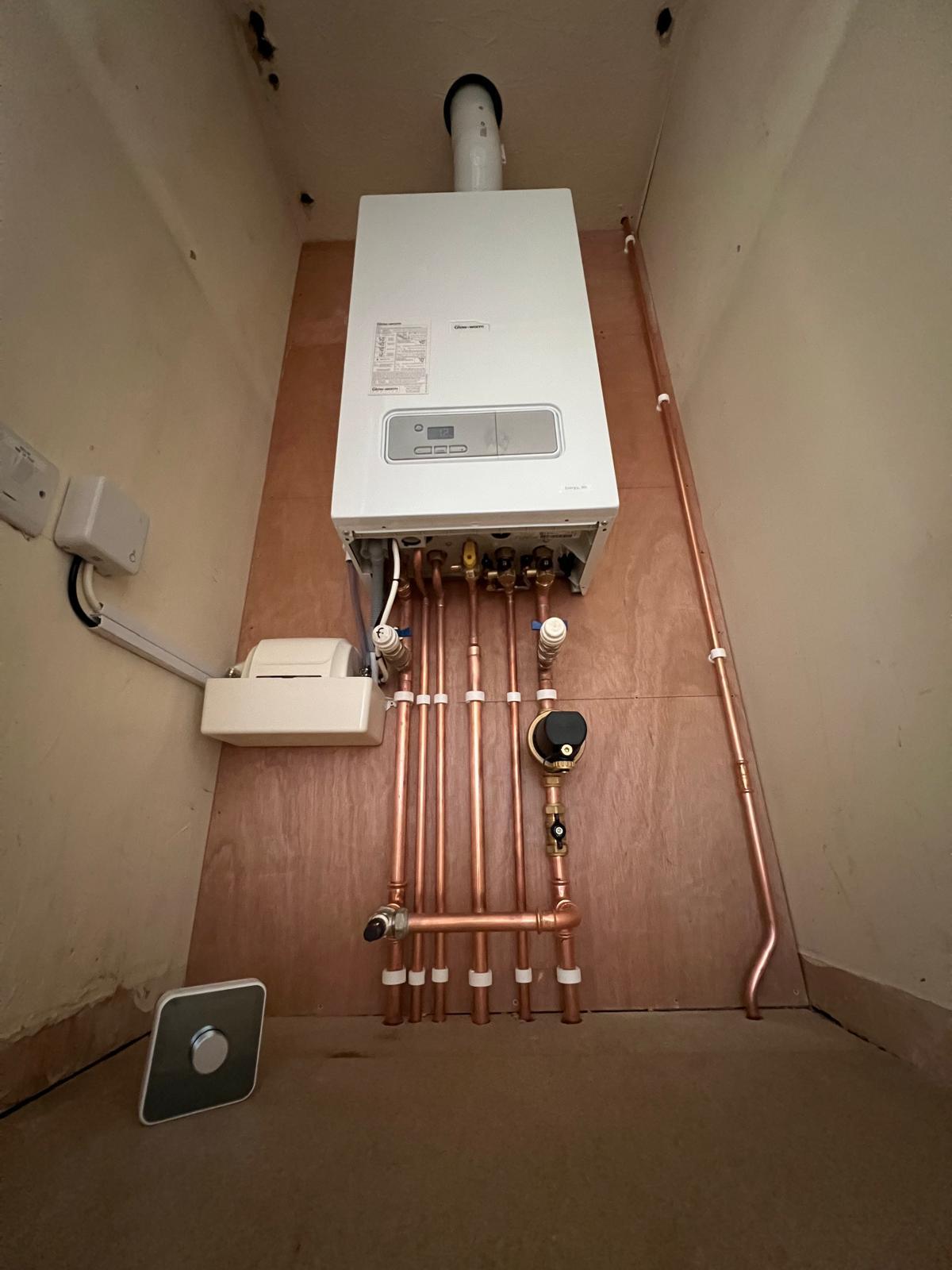 A new boiler and pipework in a plywood-lined cupboard